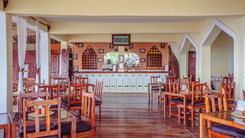 Un restaurante con sillas y mesas de madera, una barra con un cartel que dice 'Shisha Bar' y puertas de arco.