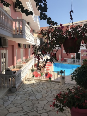 A hotel courtyard with a swimming pool, potted plants, and a staircase leading to the upper floors. - Villa Antonis (Parga)