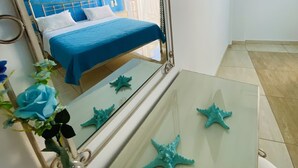 A bedroom with a large mirror, a bed with blue bedding, a TV mounted on the wall, and a small table with starfish decorations. - Villa Antonis (Parga)