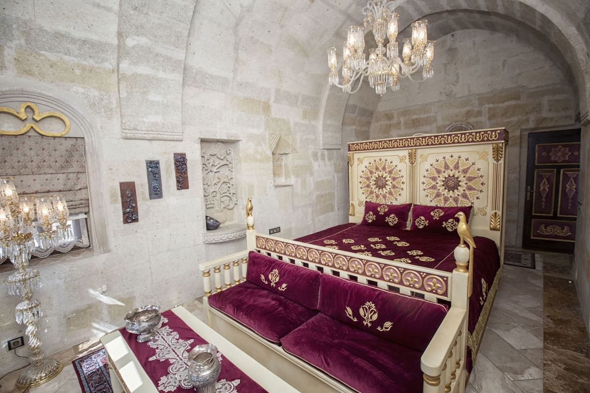 A luxurious bedroom with a large bed, ornate headboard, and a chandelier.