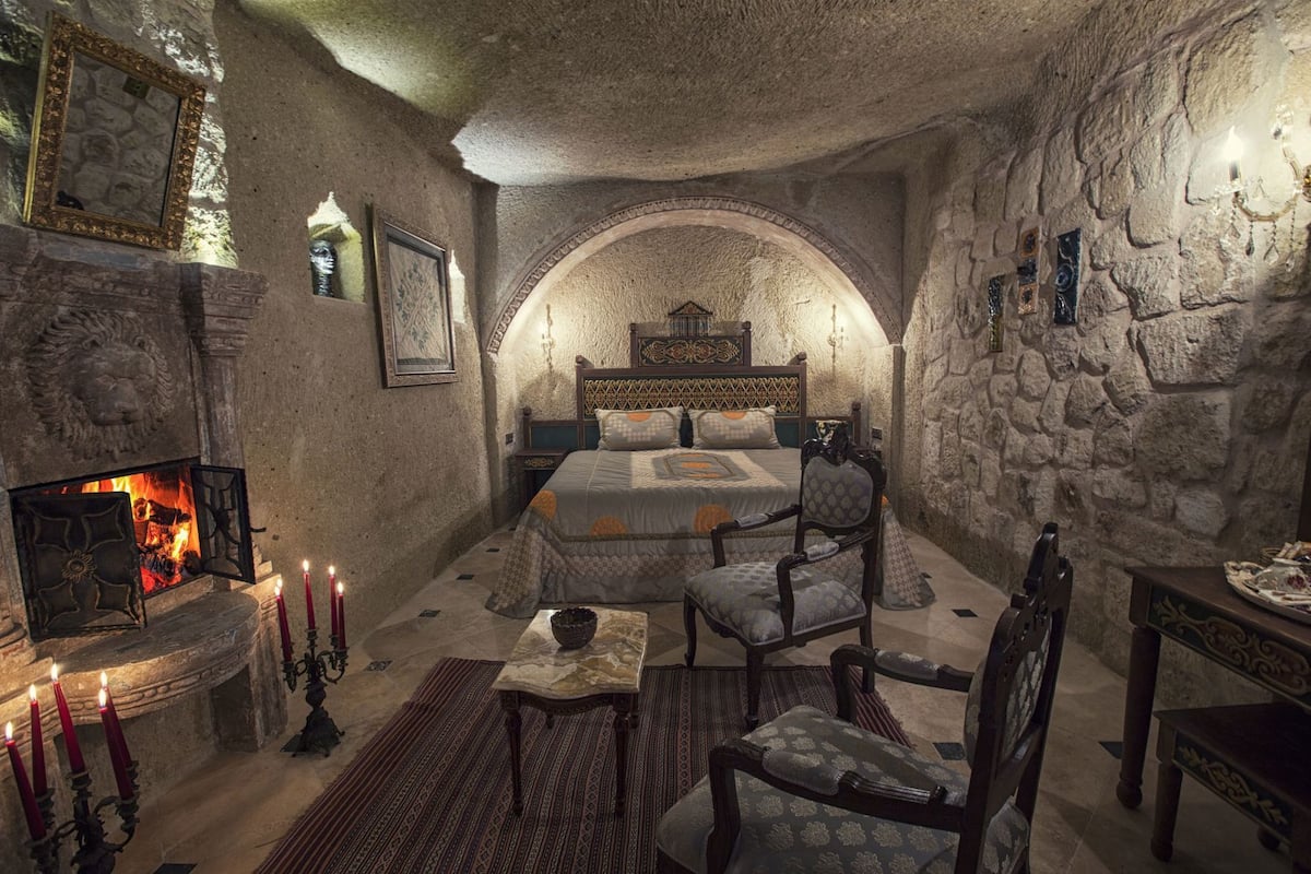 A stone-walled bedroom with a fireplace, a bed, a chair, and a table.