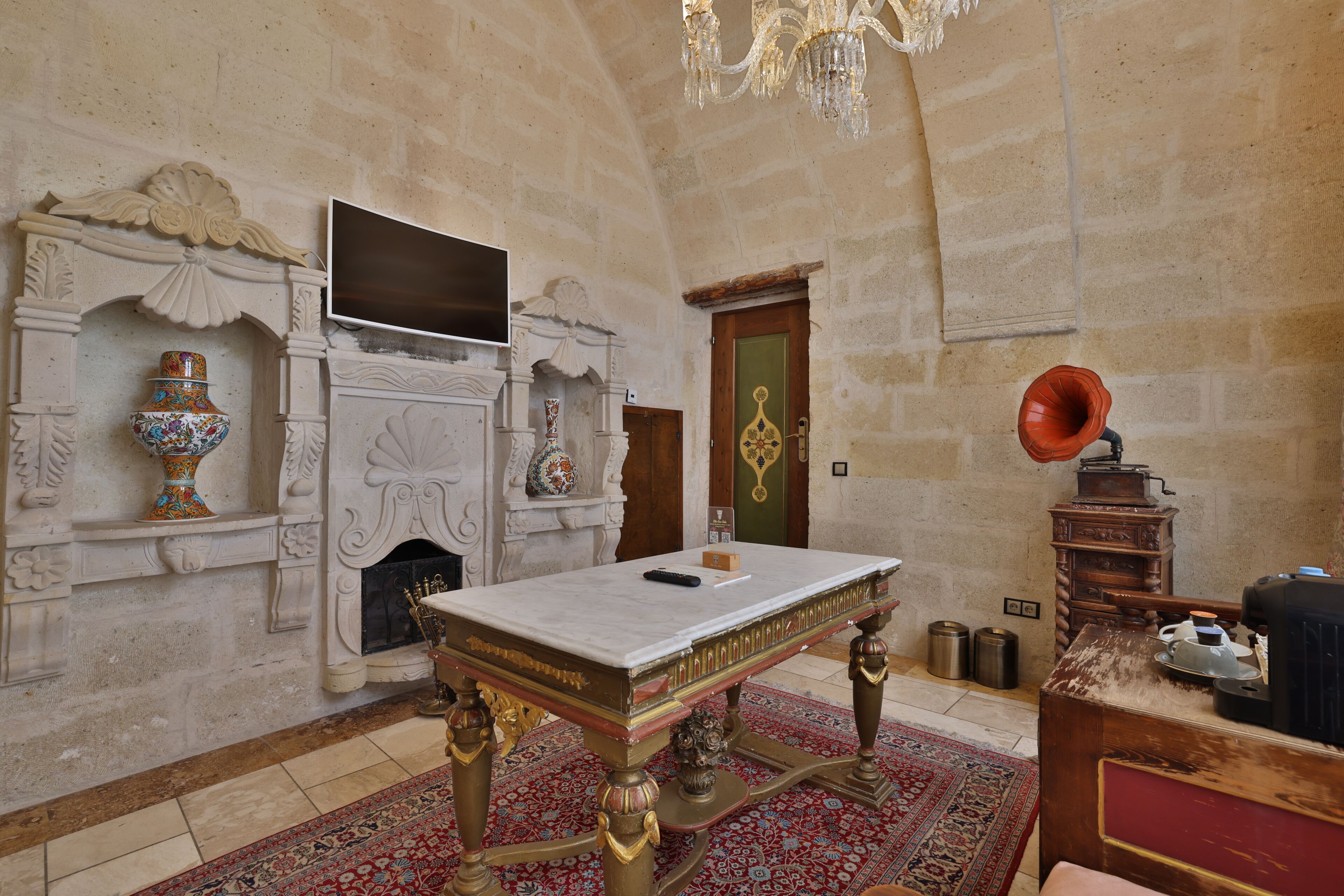 Una habitación con una mesa de mármol, chimenea, candelabro y un tocadiscos antiguo.