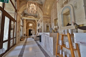 Un hall d’hôtel doté d’un comptoir de réception en marbre, d’un lustre et d’un miroir orné d’un cadre décoratif.