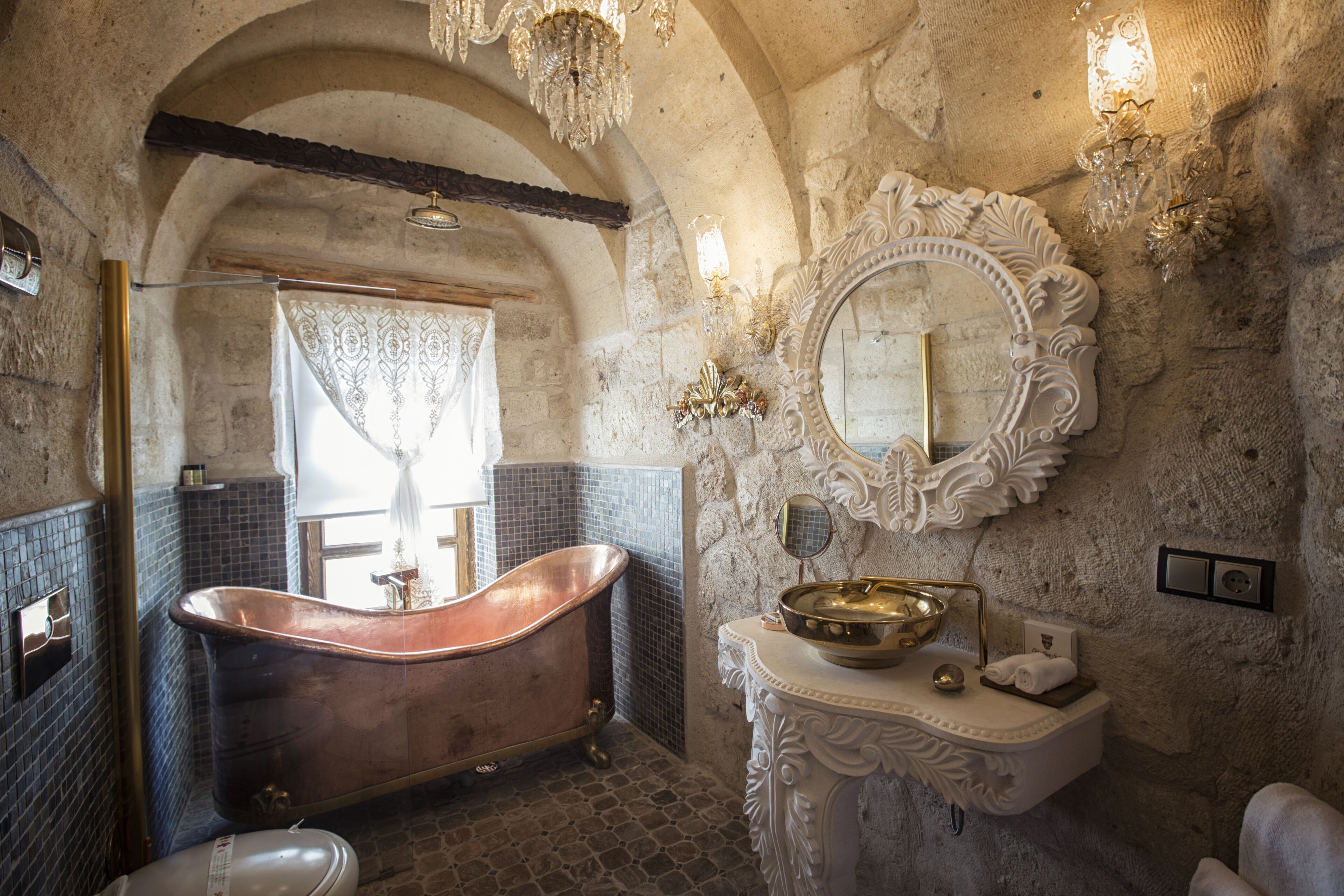 A vintage bathroom with a freestanding bathtub, a large ornate mirror, and a stone wall.