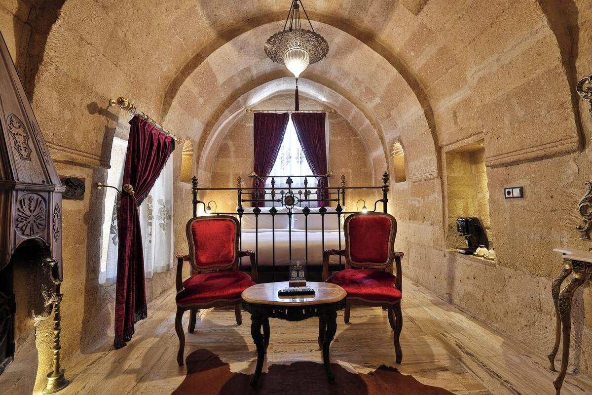 An arched room with a bed, two red chairs, a table, and a chandelier.