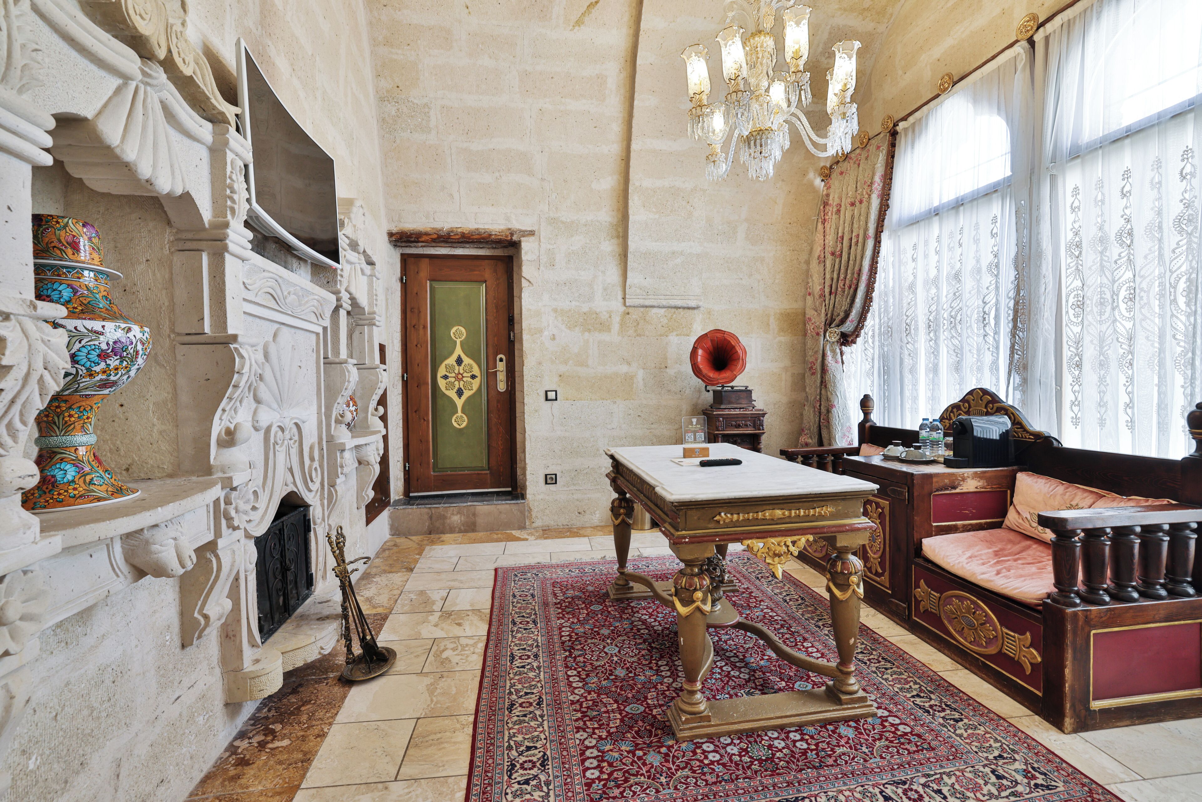 Una habitación con chimenea, muebles ornamentales, un candelabro y un amplio ventanal con cortinas.
