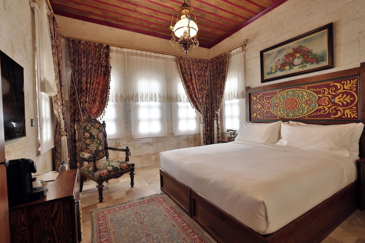 A bedroom with a large bed, a chair, a desk, and a painting on the wall.