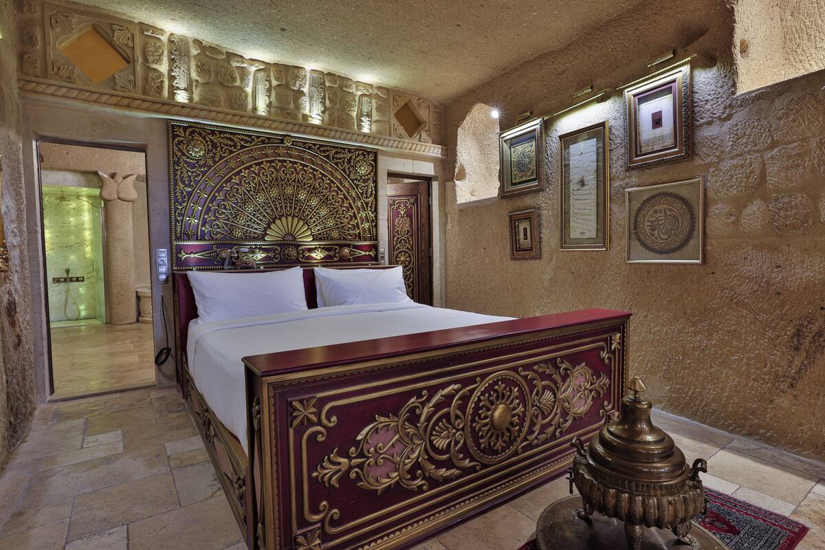 A room with a bed, a decorative headboard, a wall-mounted lamp, and framed pictures.