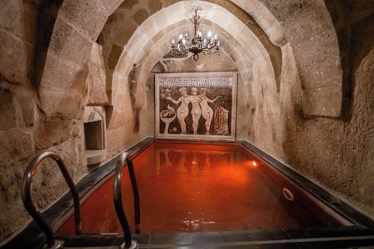 An arched stone structure with a pool, a chandelier, and a wall with a relief sculpture.