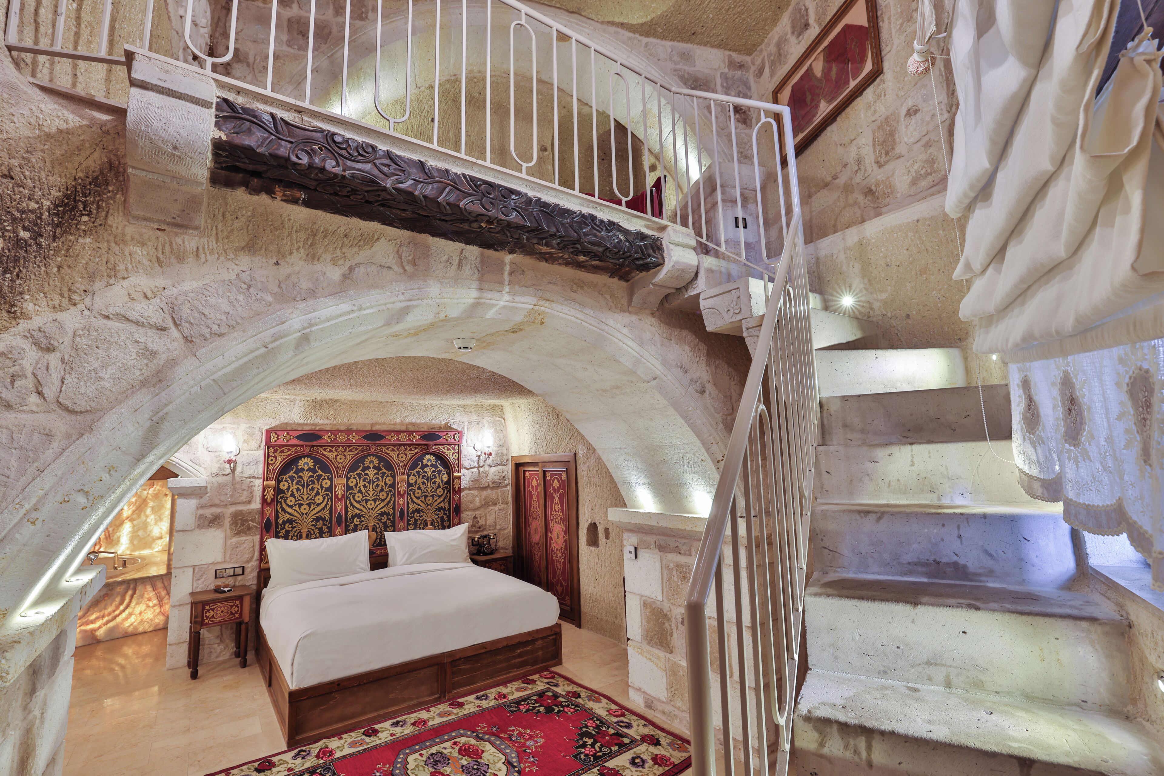 Un dormitorio con una cama grande, cabecera de madera, alfombra roja y una escalera con barandilla blanca.