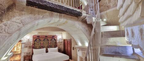 Un dormitorio con una cama grande, cabecera de madera, alfombra roja y una escalera con barandilla blanca.