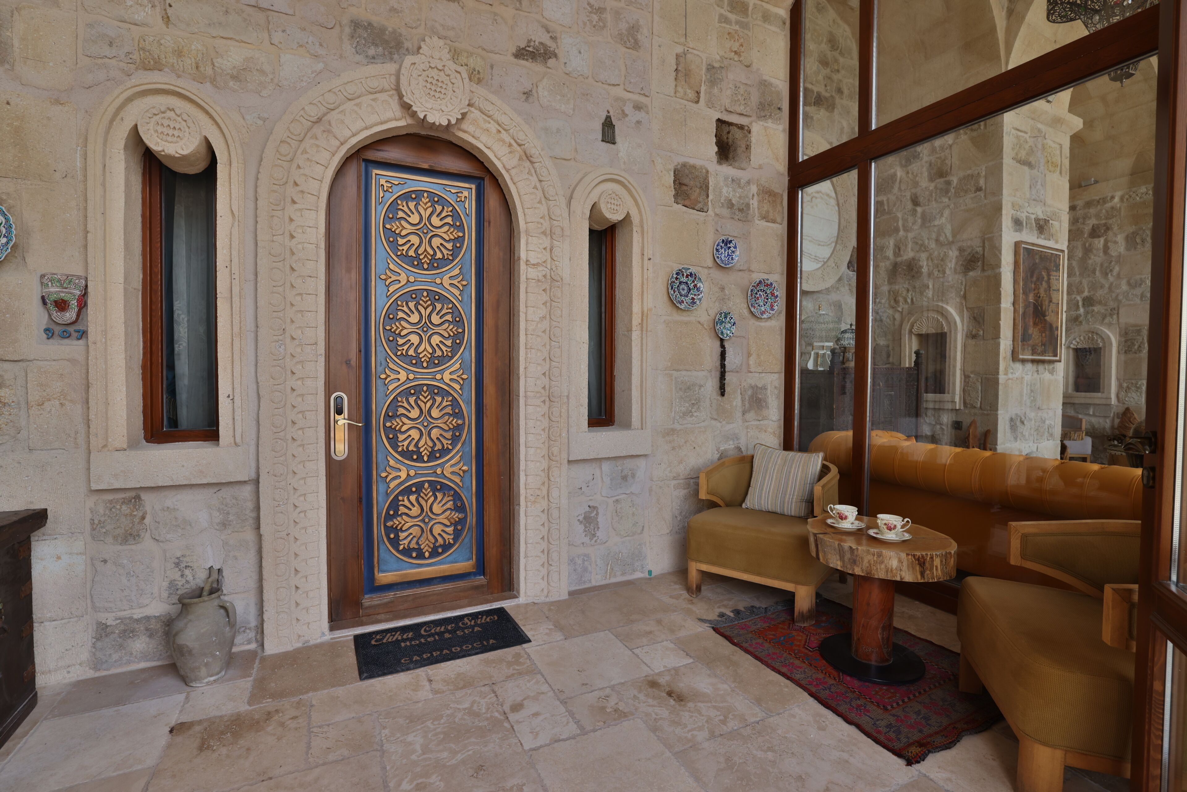 A stone-walled lobby with a blue door, a sofa, a small round table, and a tiled floor.
