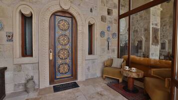 A stone-walled lobby with a blue door, a sofa, a small round table, and a tiled floor.