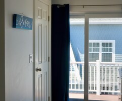 Una habitación con una puerta blanca, un letrero azul que dice 'Relax' y vistas de un edificio con fachada azul y ventanas blancas.