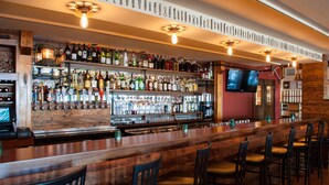 A bar with a long counter, multiple shelves of bottles, and several chairs. - Inn on the Blues (York Beach)