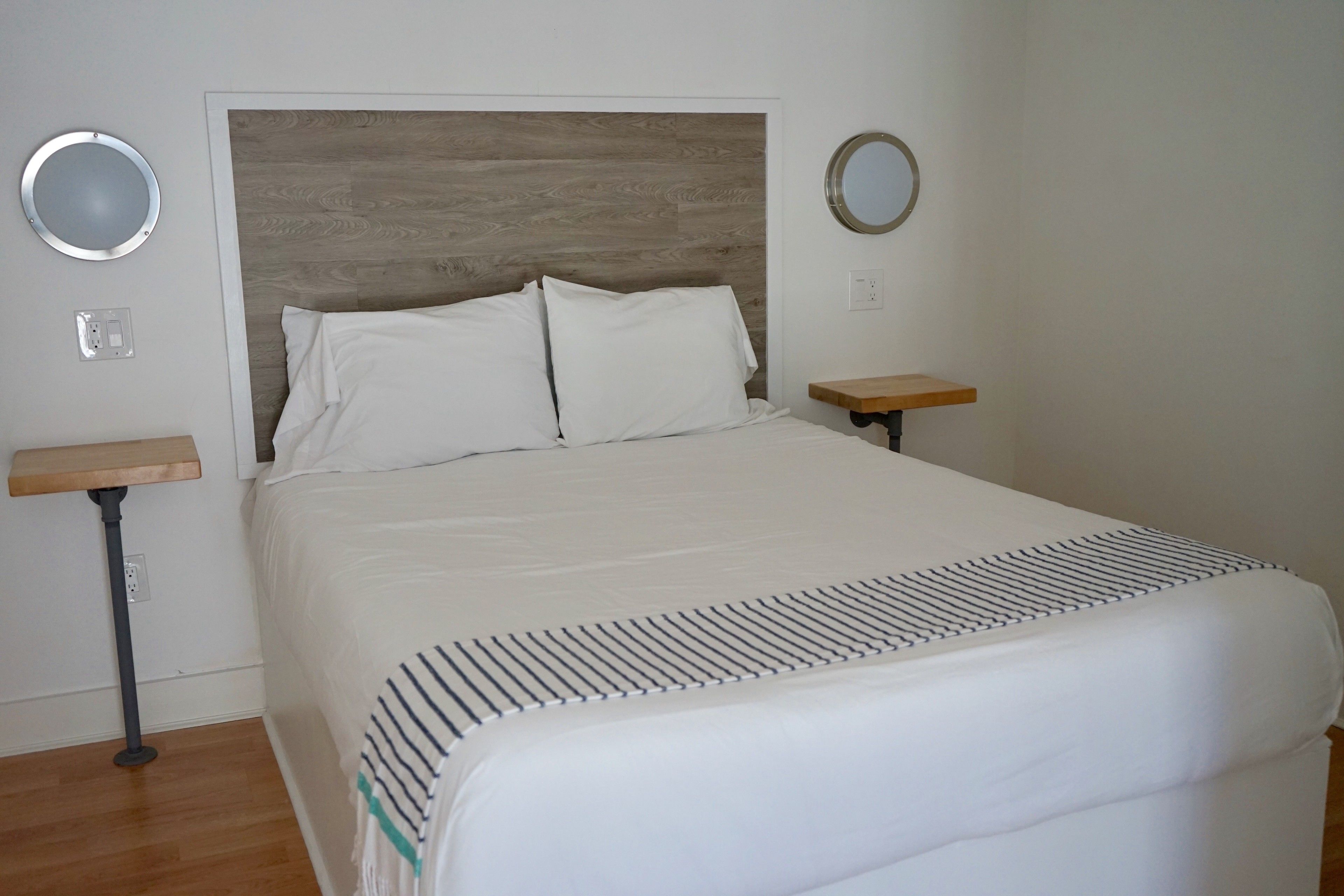 A neatly made bed with a wooden headboard, two bedside tables, and two wall-mounted mirrors.