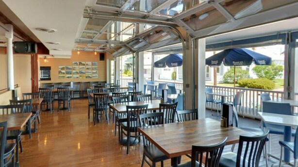 An indoor dining area with wooden tables and chairs, large windows, and blue umbrellas. - Inn on the Blues (York Beach)