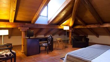 Une chambre à coucher aménagée dans un espace sous les toits, avec un plafond en pente, un bureau, une chaise, un lit et une petite table.
