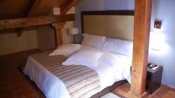 A bedroom with a large bed, wooden beams, a nightstand, and a wall-mounted lamp.