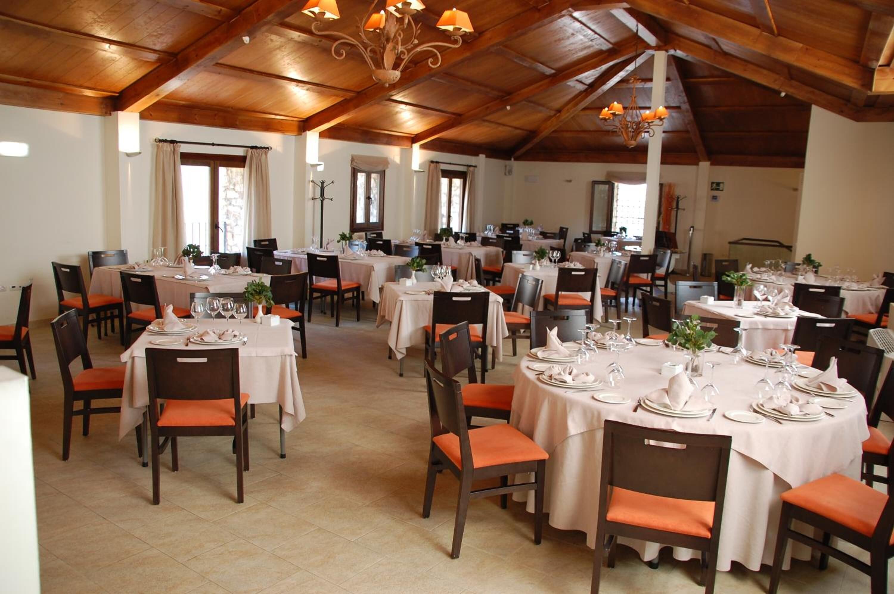 A spacious dining hall with multiple round tables set for dining, each with white tablecloths and orange chairs.