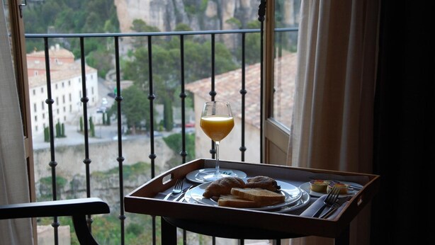 A balcony with a table set for breakfast, including croissants, toast, and orange juice, overlooking a cityscape. - Hotel Convento del Giraldo (Cuenca)