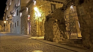 A stone building with a large arched entrance and a metal gate, surrounded by cobblestone streets and illuminated by street lamps. - Hotel Convento del Giraldo (Cuenca)