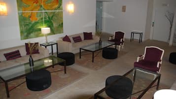 A spacious lobby with a sofa, chairs, a glass coffee table, and a large floral painting on the wall.