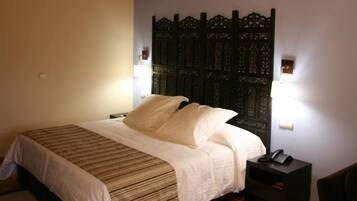 A bedroom with a wooden ceiling, a bed with white bedding, a nightstand with a phone, and a decorative headboard.