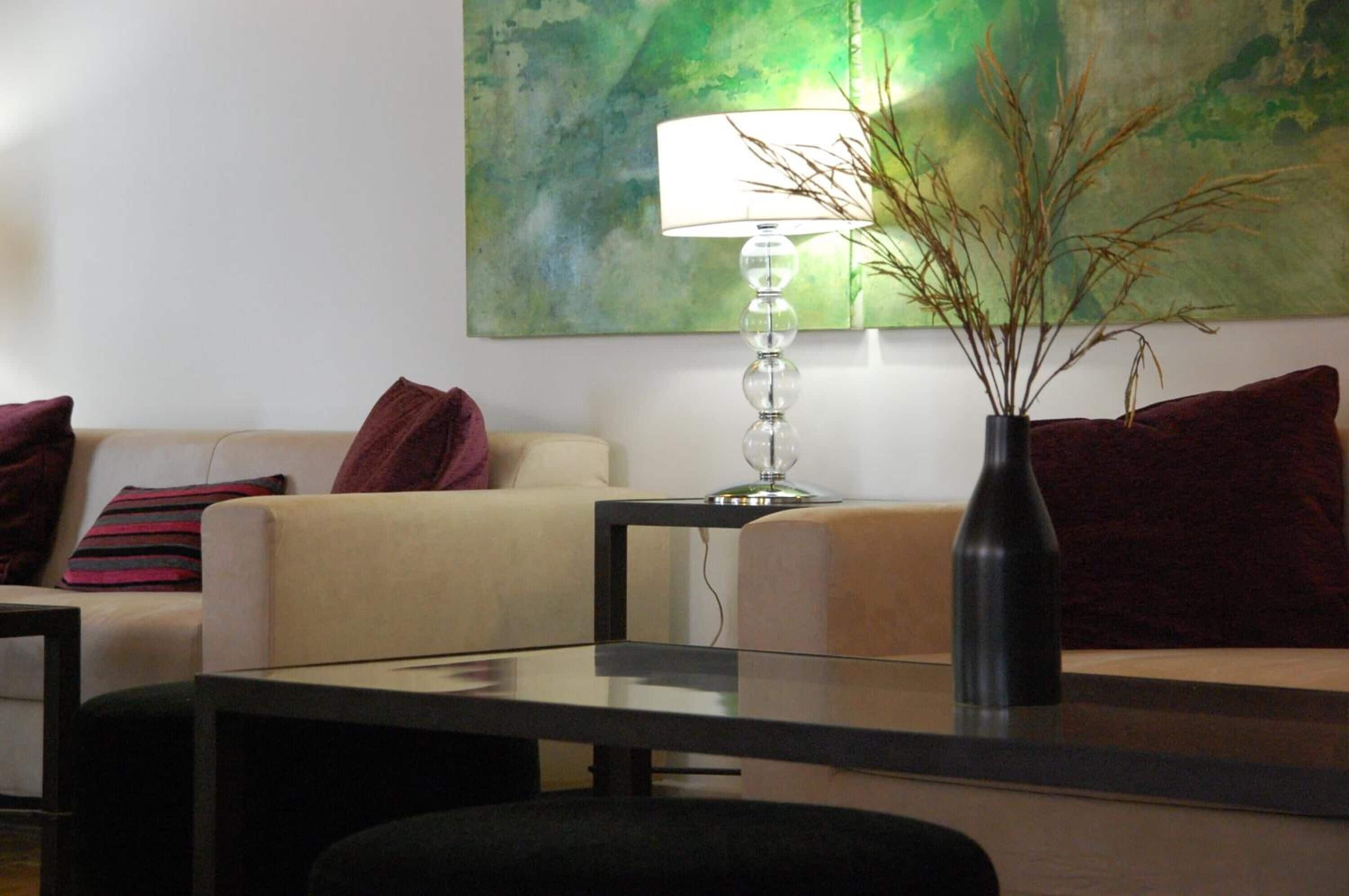 Een moderne woonkamer met een bank, een glazen salontafel, een lamp en een vaas met takken.