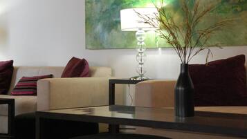 Een moderne woonkamer met een bank, een glazen salontafel, een lamp en een vaas met takken.