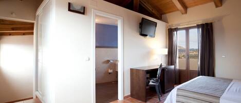 A bedroom with a bed, a desk, a television, and a view of the outdoors.