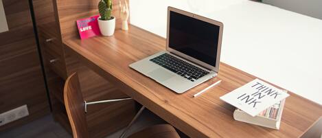 A wooden desk with a laptop, a potted plant, a small cactus, a pink sign, and a book with text.