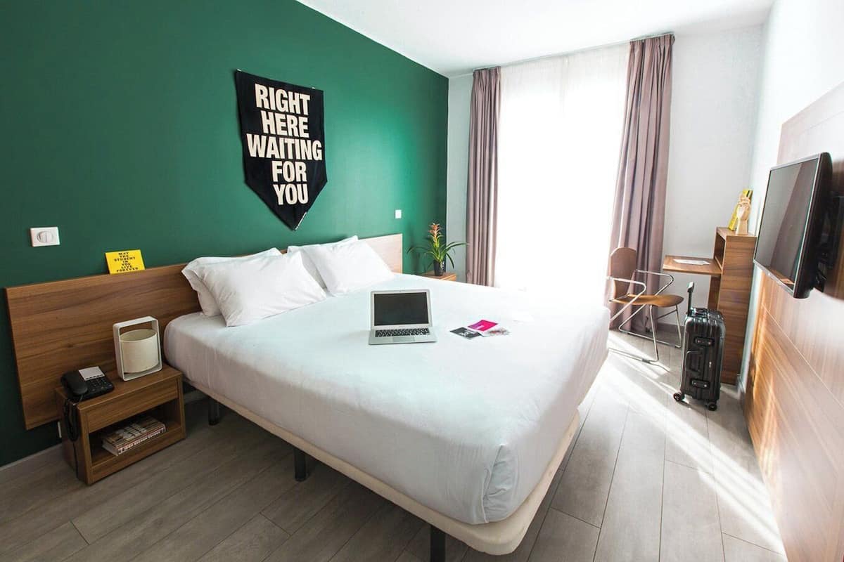 Une chambre d’hôtel avec un lit, un bureau, une chaise, une télévision et une valise.