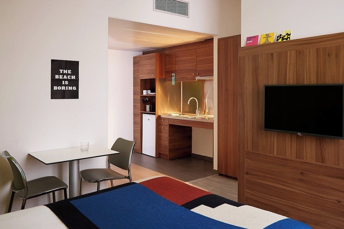 Une chambre d’hôtel moderne équipée d’un lit, d’un bureau, d’une chaise, d’une télévision et d’une kitchenette.