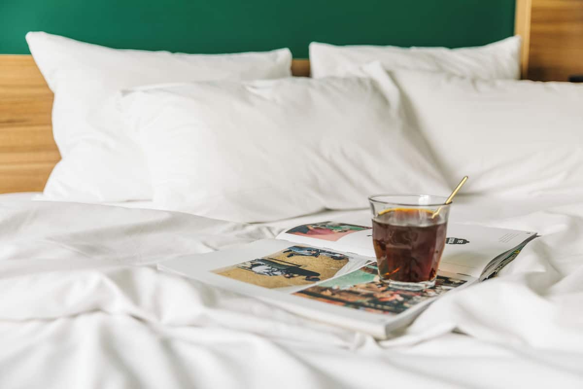Un lit avec des draps blancs, un verre de thé glacé et un magazine sur un plateau.