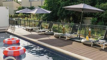 Un área junto a la piscina con sillas de descanso, sombrillas y una terraza de madera.