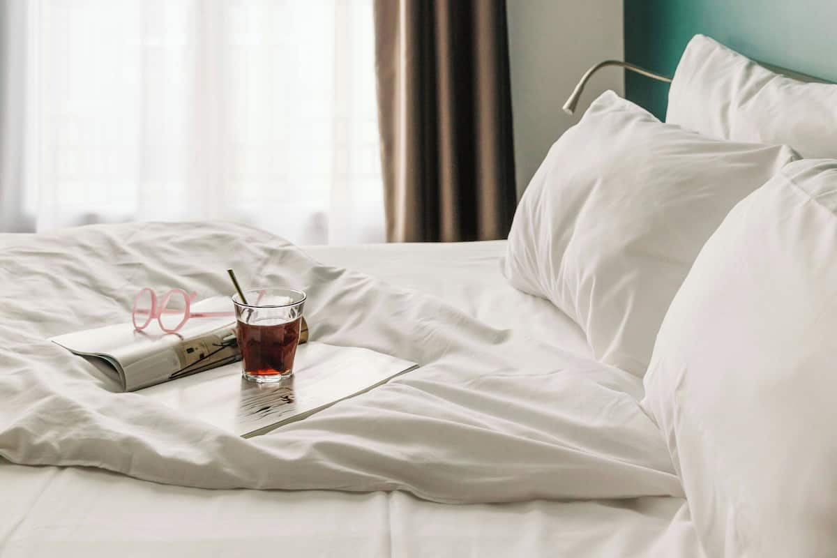 Une chambre d’hôtel avec un lit, une boisson et une paire de lunettes posées sur le lit.