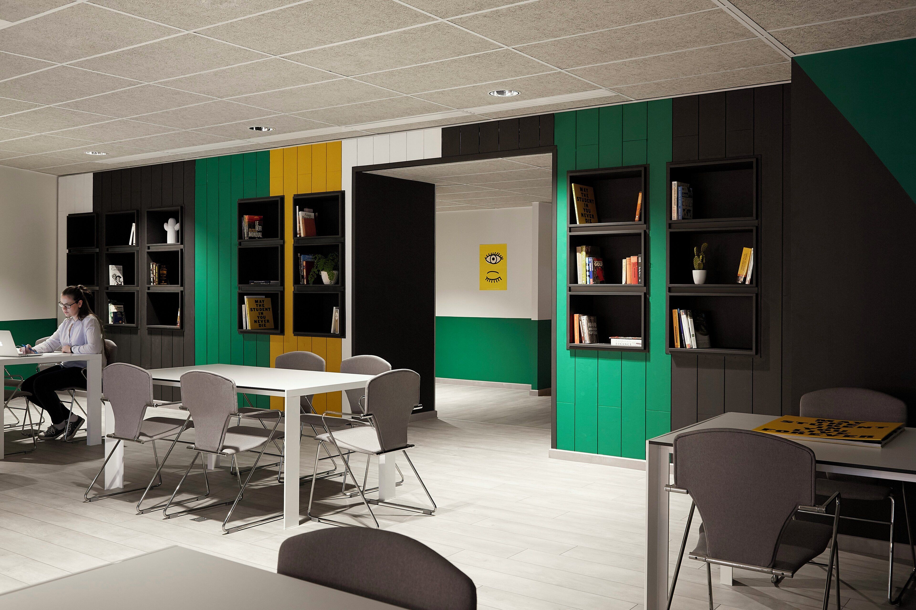 A modern office space with white tables, grey chairs, and black bookshelves.
