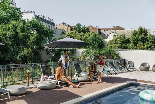 Un espace piscine aménagé sur le toit, avec des chaises longues, une piscine et une vue sur les bâtiments environnants.