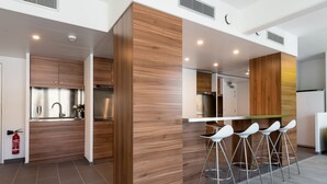 A modern kitchen with wooden cabinetry, a stainless steel refrigerator, and a bar area with white bar stools.