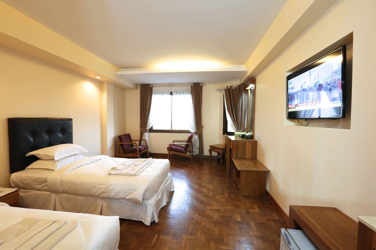 A hotel room with two beds, a TV, a desk, and a chair.