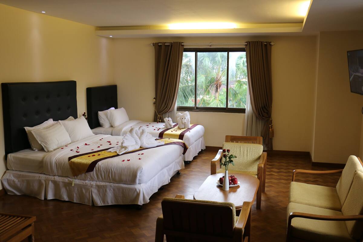 A hotel room with two beds, a dining table, a chair, and a TV.
