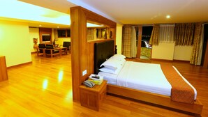 A hotel room with a large bed, wooden flooring, a desk with a chair, a small table with a basket, and a view of the city at night. - Queen's Park Hotel (Yangon)