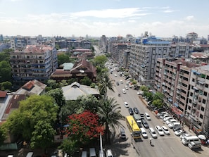 A cityscape with multi-story buildings, a busy street with cars and a bus, and a prominent red flowering tree. - Queen's Park Hotel (Yangon)