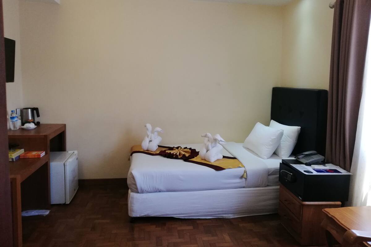 A hotel room with a bed, a desk, a refrigerator, and a window with curtains.
