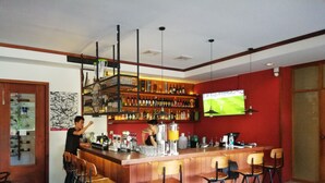 A bar area with a wooden counter, multiple stools, and shelves stocked with bottles. - Queen's Park Hotel (Yangon)