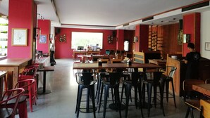 A restaurant with red walls, multiple tables and chairs, and a large window providing natural light. - Queen's Park Hotel (Yangon)