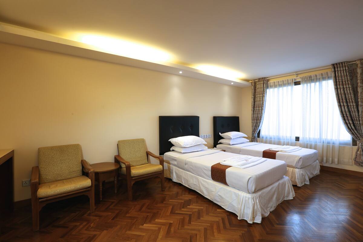 A hotel room with two single beds, a wooden chair, and a small table.
