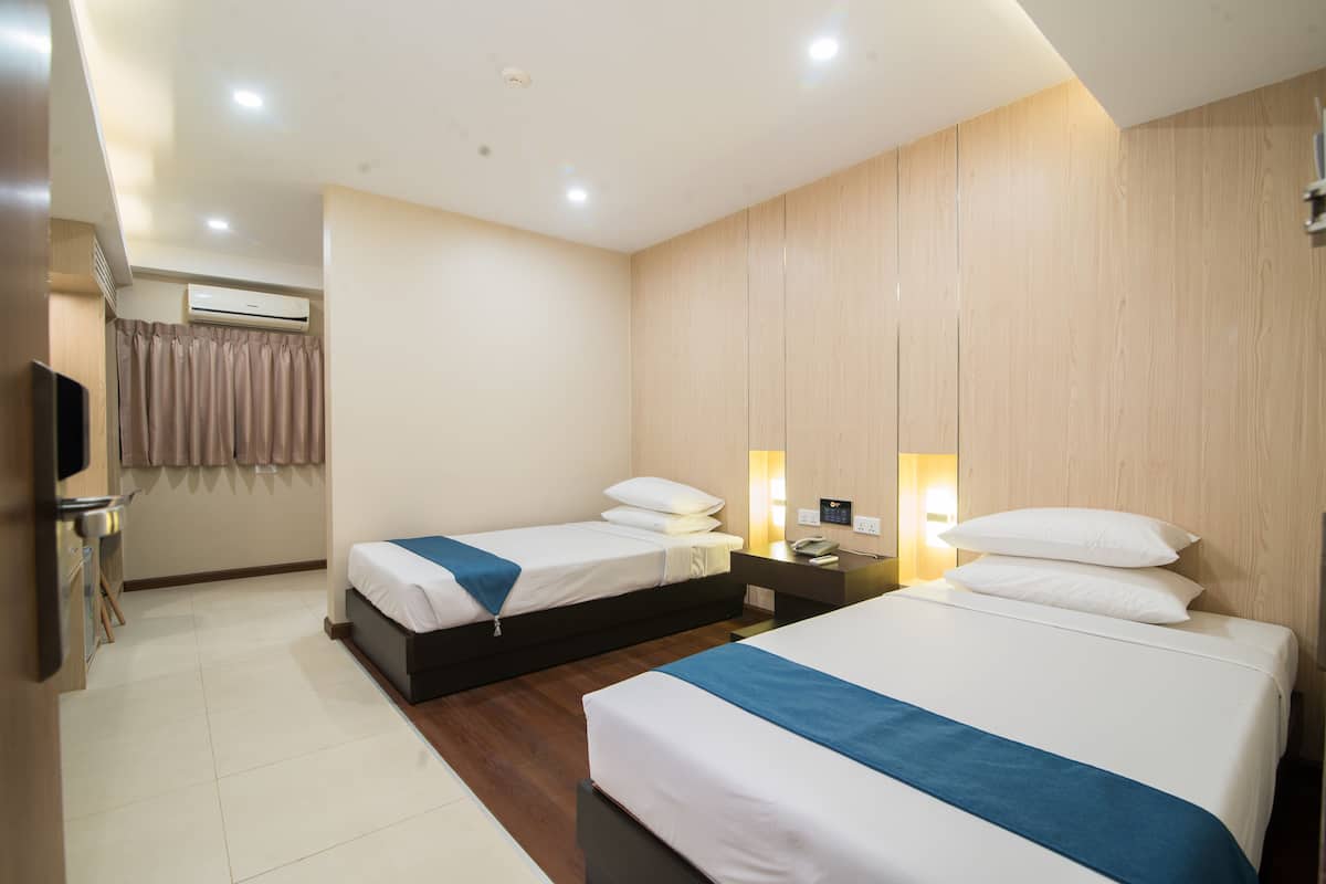 A hotel room with two beds, a desk, a TV, and an air conditioning unit.