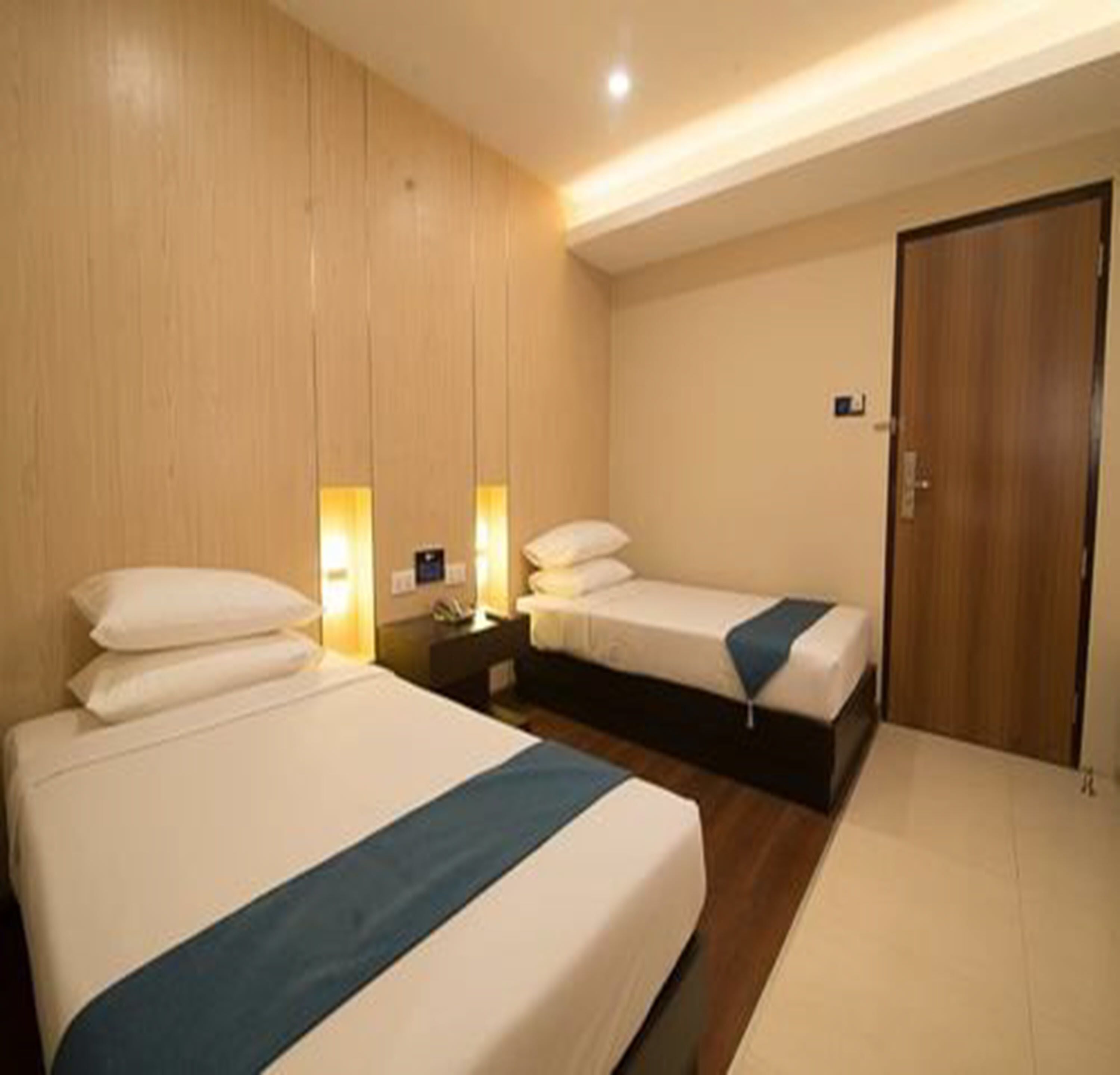 A hotel room with two beds, wooden paneling on the walls, and a door.